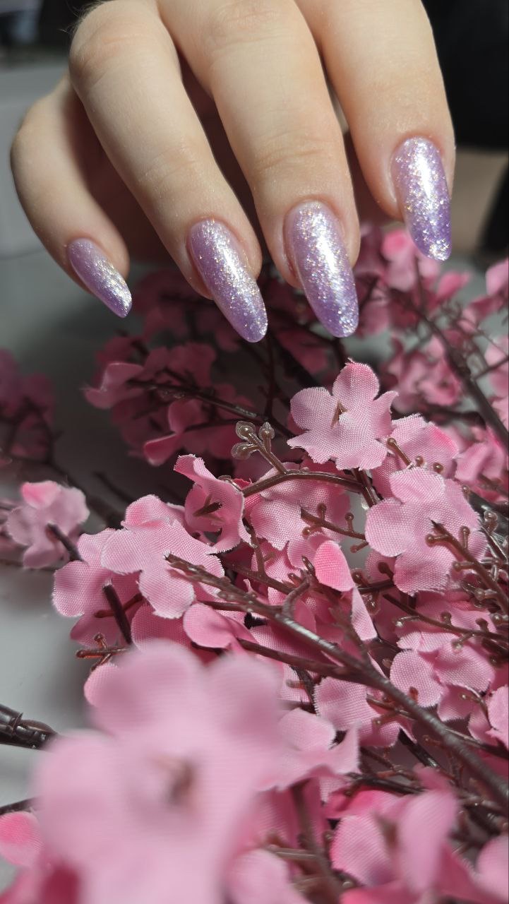 Νύχια με ροζ και μωβ glitter μπροστά από ροζ λουλούδια